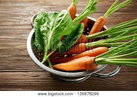 Carrots with sorrel in colander on wooden table
