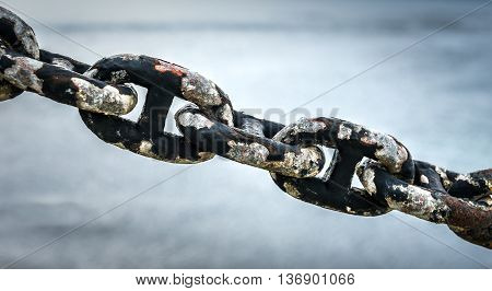 Old rusty anchor iron ship chain in sea port. Old fence made of obsolete boat chain elements with sea ocean in background.