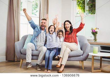 Full length of happy family cheering while siting on sofa at home