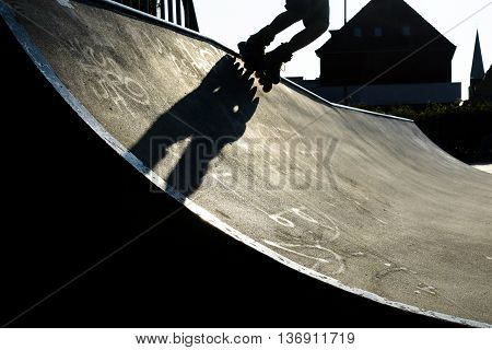 Feet of a rollerblader with inline skates riding over the concrete halfpipe in an outdoor skate park dramatic backlit shot with hard shadows nearly black and white copy space selected focus motion blur