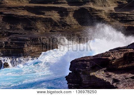 Ocean Waves Crashing against rocks and cliffs with white foam Close-up. Rustic weathered lava rock cliff face