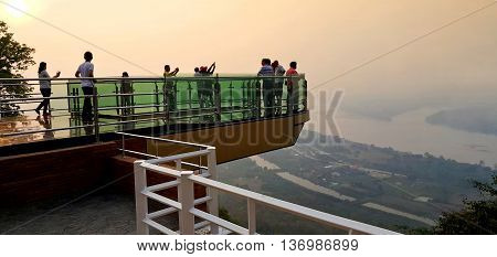 Nong Khai province Thailand- April 28 2016: Tourists walking and taking photograph on transparent sky walk to see view of Mekong River during sunset at Wat Pha Tak Suea Sangkhom district Nong Khai province Thailand.