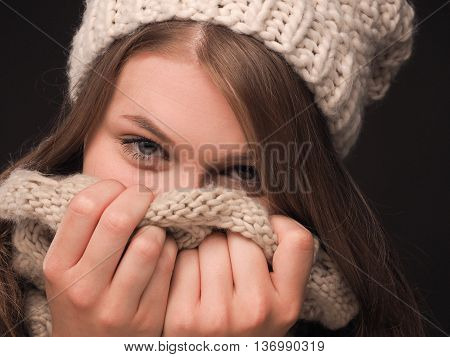 Close up portrait of a beautiful teenage girl dressed with wool cap and scarf on a gark background