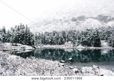 Mirror Surface Of The Winter Lake With A Mountain Range. First Snow In The Mountains. Travel To The