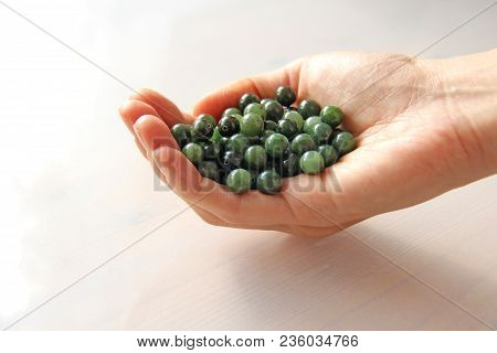 Natural Green Jade Nephrite Mineral Stones Beads. The Green Jade Stone Lies In The Hands. Hands Hold