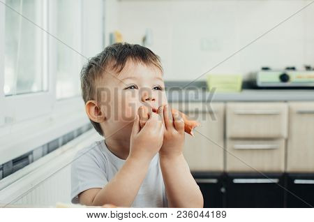 Handsome Boy Shaggy And Shkod Eats Sausage In The Kitchen In A White T-shirt In The Afternoon