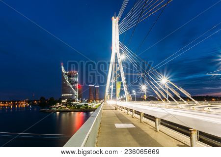 Riga, Latvia. Vansu Cable-stayed Bridge In Bright Night Illumination Over The Daugava River, Skyscra