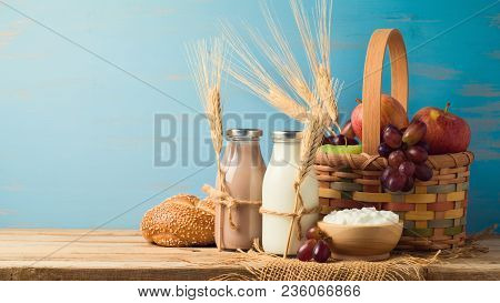 Milk, Chocolate Milk Bottles And Basket With Fruits On Wooden Table. Jewish Holiday Shavuot Concept.