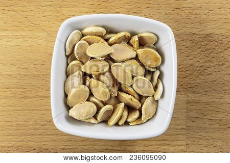 Overhead Shot Of Raw Shelled Pumpkin Seeds In A White Bowl On A Wooden Chopping Board Background. Mo