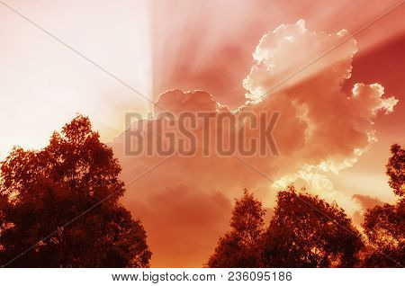 An Abstract Image Of Sun Light Beams Escaping Behiind Large Reddish White Puffy Clouds In Vietnam In