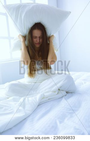 Young caucasian woman covering her head and ears with pillows