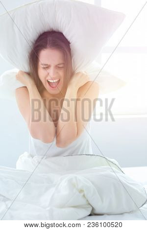 Young caucasian woman covering her head and ears with pillows