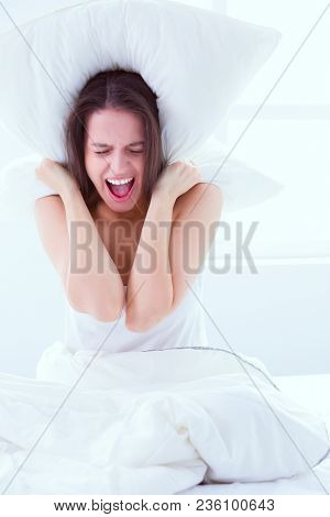 Young caucasian woman covering her head and ears with pillows