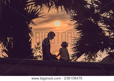 Silhouettes Of The Father And Son, Who Meet The Sunset In The Tropics Against The Backdrop Of Palm T