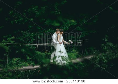 The Bride And Groom Posing On A Suspension Bridge