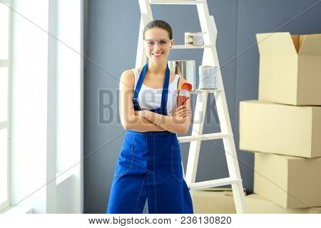 Happy beautiful young woman doing wall painting, standing near ladder