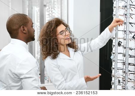 Young Doctor Helping To Choose Right Eyelense In The Ophthalmology Laboratory. Looking Expirienced A