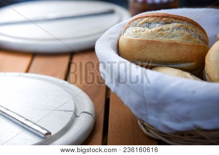 Basket Of Freshly Baked Dinner Rolls With Tableware In Background. Close Up