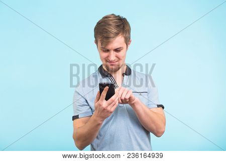 Young Man Texting Message On Smart Phone Isolated On Blue Background. Smiling Guy Holding Smartphone
