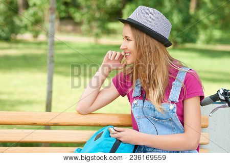 Sideview Of Smiling Girl Sitting On Wooden Bench In City Park. Feeling Positive, Relaxed, Happy. Spe