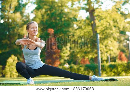 Frontview Of Girl Doing Stretching On The Park's Grass.