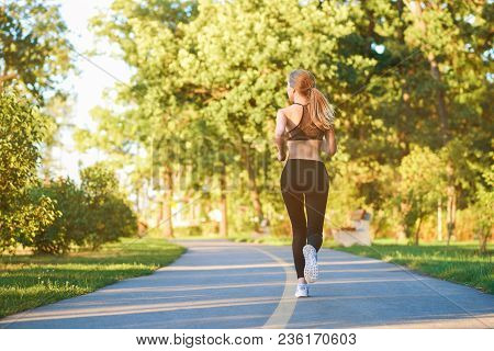 Backview Of Sporty Girl Running Along Racetrack In The City Park. Having Slim Body, Stunning Figure,