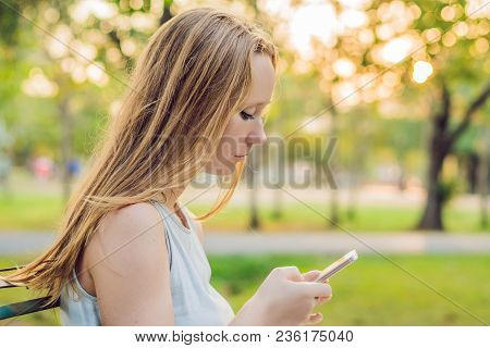 Young Calm Girl Using Her Mobile Phone To Send A Text While Standing In A Park.