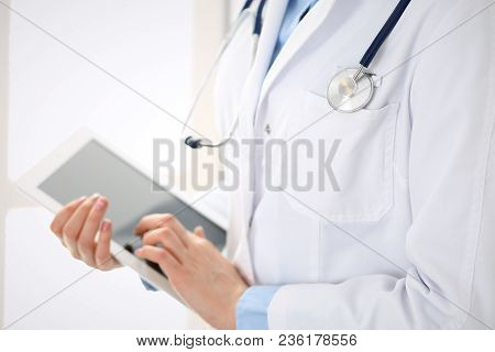 Woman Doctor Using Tablet Computer While Standing Straight In Hospital Closeup. Healthcare, Insuranc