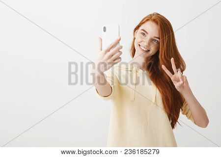Say Hi To Technology. Studio Portrait Of Beautiful Caucasian Girl With Ginger Hair Taking Selfie On 