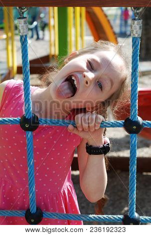 Little Girl In Pink Dress Showing Tongue While Playing Outdoor At Playground. Close Up Portret Of A 