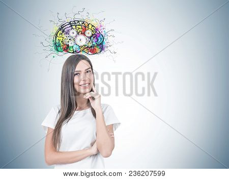 Smiling Young Woman With Fair Hair Wearing A White T Shirt And Thinking While Looking At The Viewer.