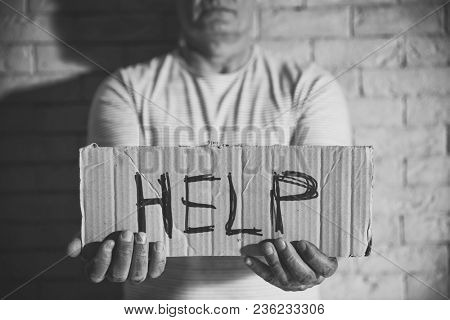 Poor man holding sign with word HELP on brick wall background. Black and white effect