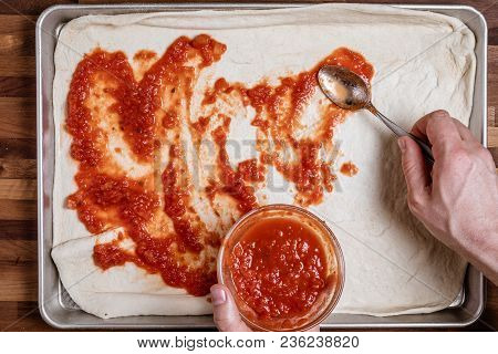 Man Spreading Tomato Sauce On Rolled Out Dough For Homemade Pizza