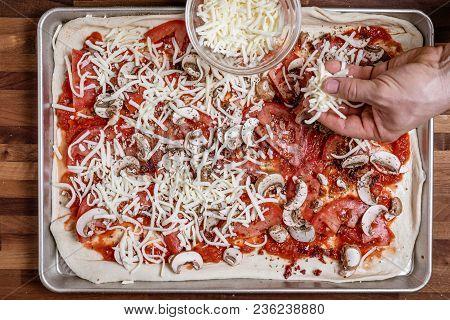 Man Spreading Shredded Cheddar Cheese On To Homemade Pizza