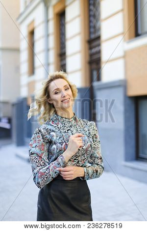 Pretty Woman Standing Near Building In Background And Wearing Leather Skirt. Oncept Of Vogue And Fas