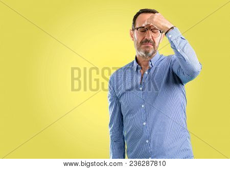 Handsome middle age man with sleepy expression, being overworked and tired, rubbes nose because of weariness