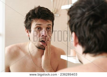 Tired Man Who Has Just Woken Up Looks At His Reflection In The Mirror Slaps His Cheek With His Hand