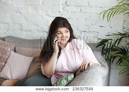 Beautiful Positive Chubby Young Woman Smiling Happily While Speaking On Smart Phone Indoors, Gossipi