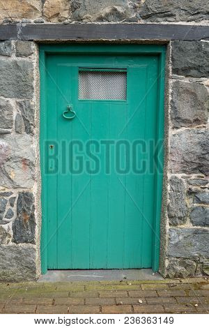 A Green Door With Grill And Lever Latch Handle Set In A Stone Wall With Slate Lintel.