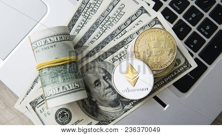 Ethereum And Bitcoin Cryptocurrency On Top Of 100 Dollar Biils On A Laptop. Profit From Mining Crypt