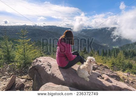 Young Brunette Woman With Her Bichon Havanese Dog Sitting On A Rock Admiring The Hornisgrinde Mounta