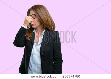 Middle age business woman with sleepy expression, being overworked and tired, rubbes nose because of weariness