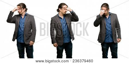 Handsome young man with sleepy expression, being overworked and tired, rubbes nose because of weariness