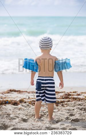 Back View On Cute Toddler Boy Wearing Safety Inflatable Armbands Standing On The Beach Ready To Jump