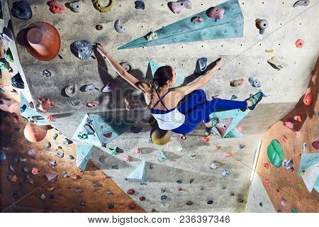 Workout Exercise. Woman Climber Climbs Indoors In Bouldering Gym. Young Woman Climbing Up On Practic