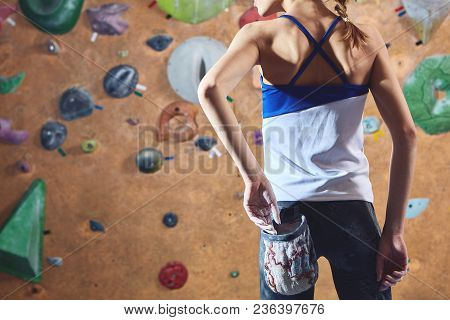 Woman Climber Preparing To Climb Indoors In Bouldering Gym With Dramatic Light. Woman Using Chalk. A
