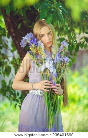 Attractive Young Girl With Blonde Dren Hair And Natural Make-up Smelling Blue Purple Iris Flowers On