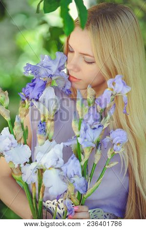 Attractive Young Girl With Blonde Dren Hair And Natural Make-up Smelling Blue Purple Iris Flowers On