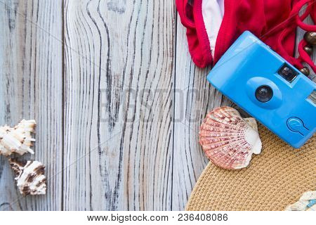 Vacation Concept. A Camera, Red Swim Suit And Sea Shells On A Grey Wooden Background, Copy Space
