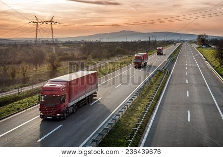 Caravan Or Convoy Of Red Lorry Trucks In Line On A Country Highway